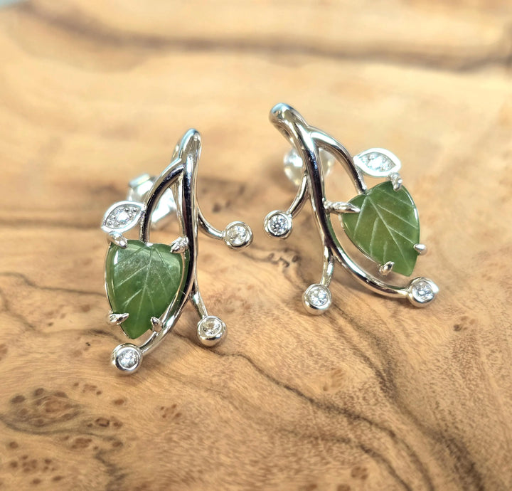 Canadian Jade Leaf and Silver Earrings feature a green jade leaf held by curling silver vines with crystal accents on a wood surface