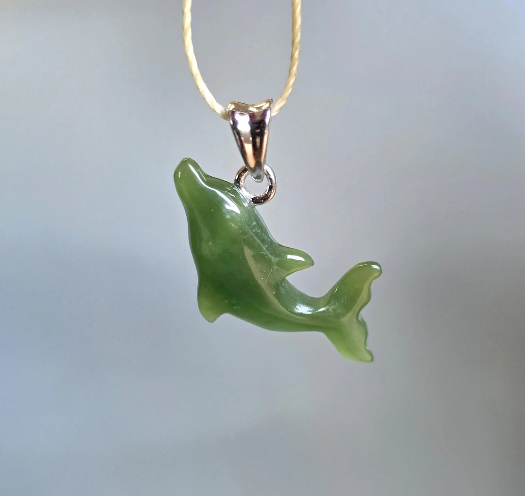 Green dolphin shaped pendant carved from jade-like stone on a beige cord necklace.