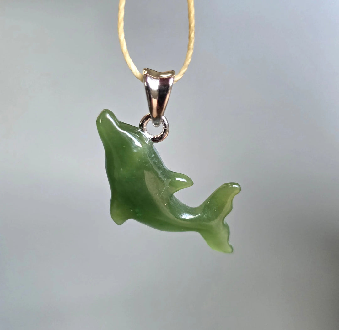 Green jade dolphin pendant with a silver bail suspended from a cream cord necklace