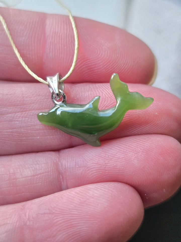 Close up of a green dolphin pendant on a light cord being held between fingers.
