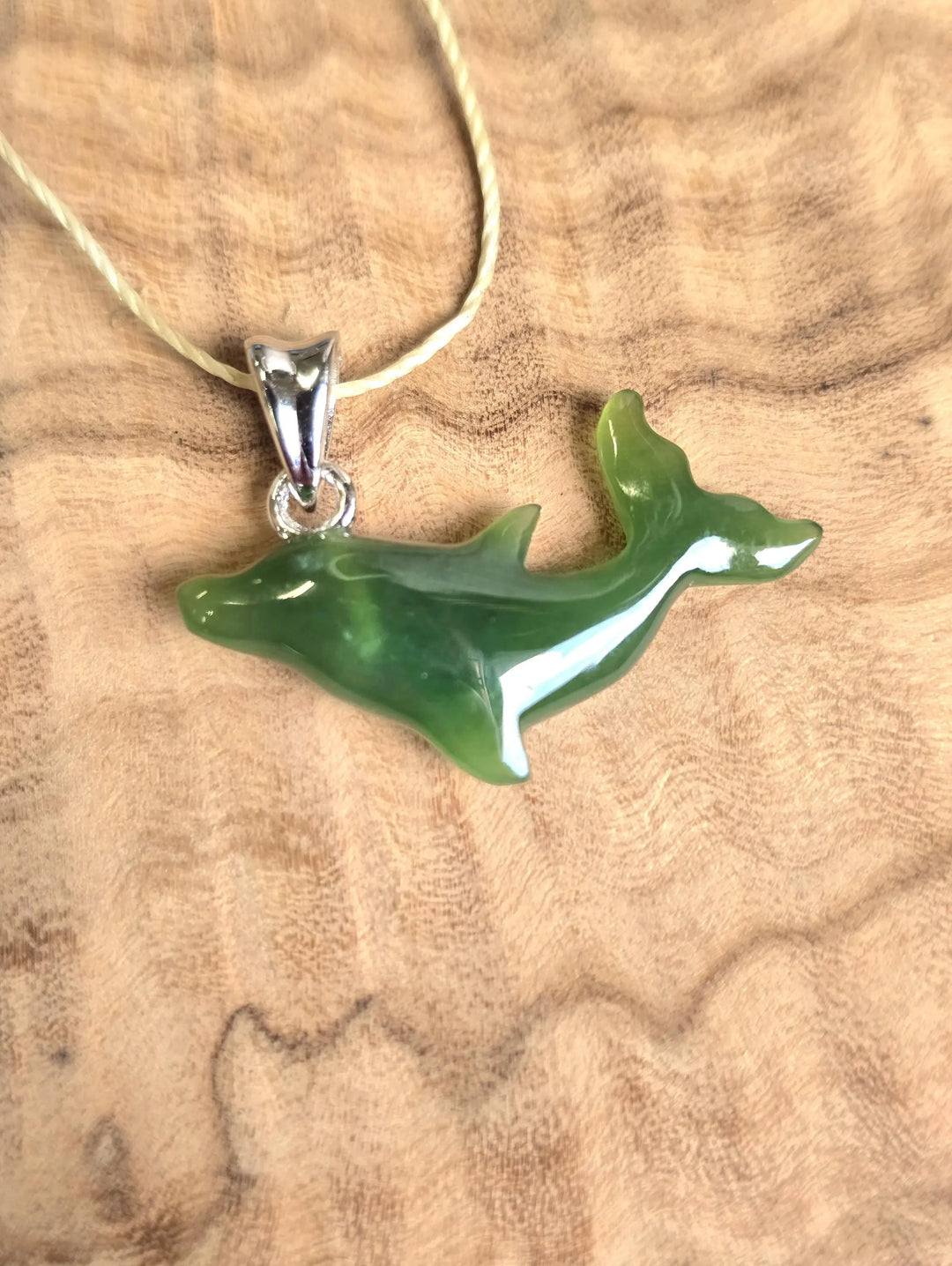 Green jade dolphin pendant with a silver bail on a beige cord necklace