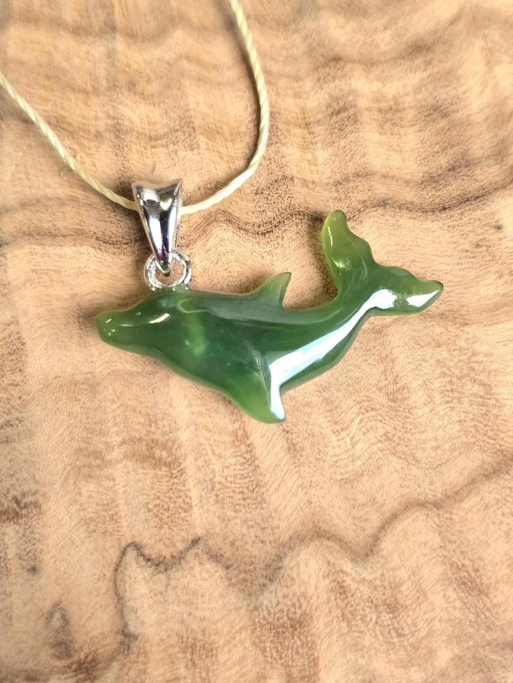 Green jade dolphin pendant with a silver bail on a beige cord necklace