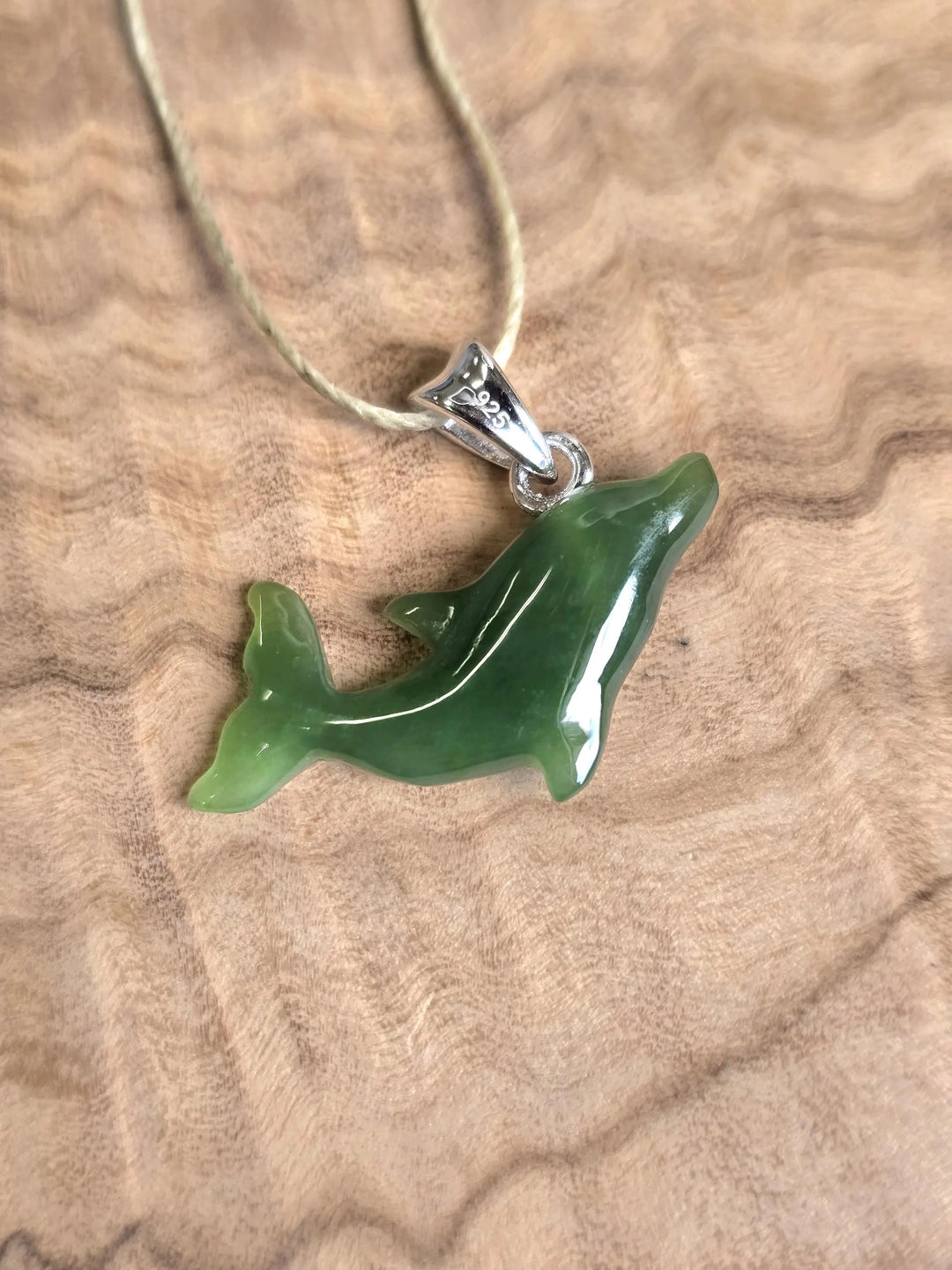 Dolphin shaped pendant on a light cord with a silver bail resting on a wood surface.