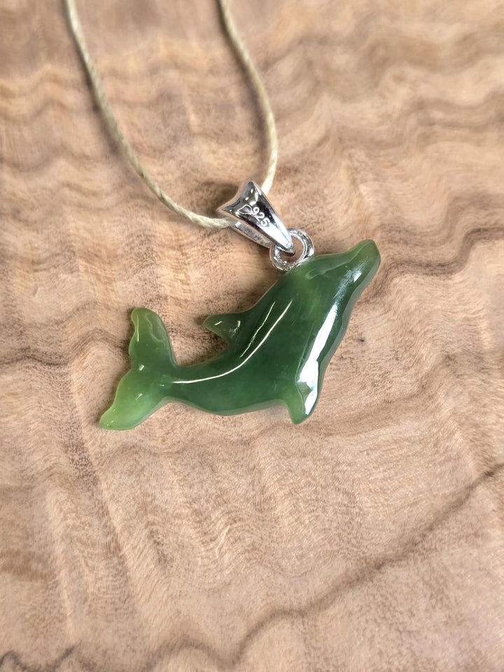 Dolphin shaped pendant on a light cord with a silver bail resting on a wood surface.
