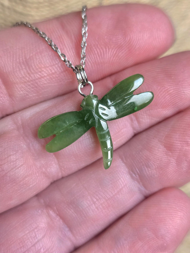 Green jade dragonfly pendant on a silver chain held in a hand