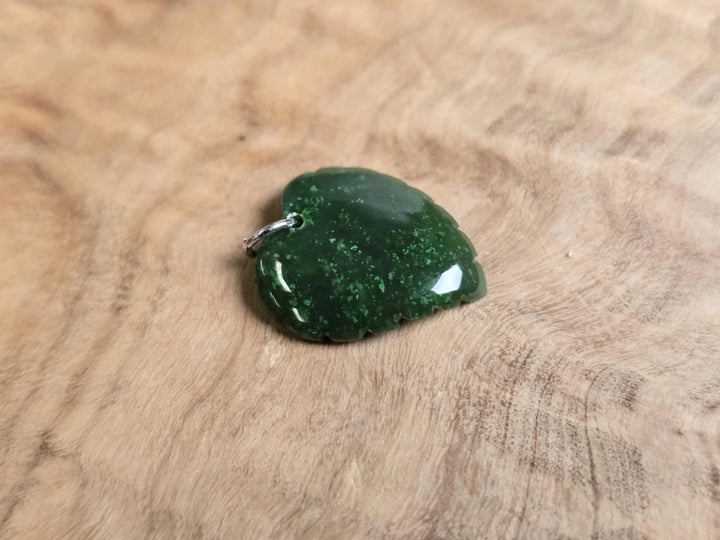 Dark green jade leaf pendant with a metal bail on a wooden background.