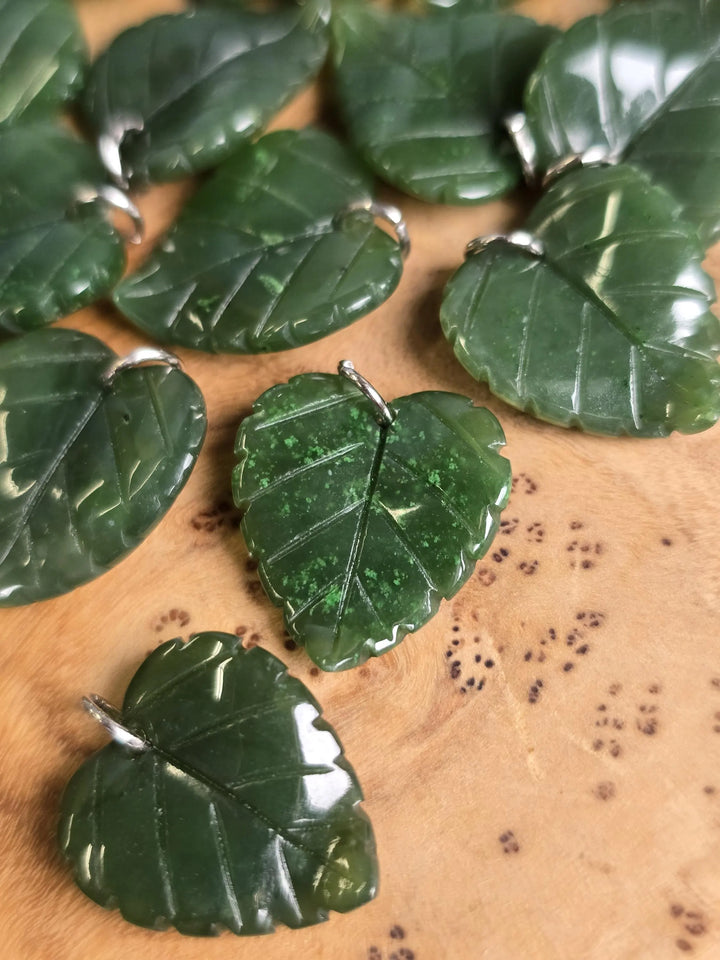 Assorted Canadian Jade leaf charms with silver bails scattered on a wooden surface