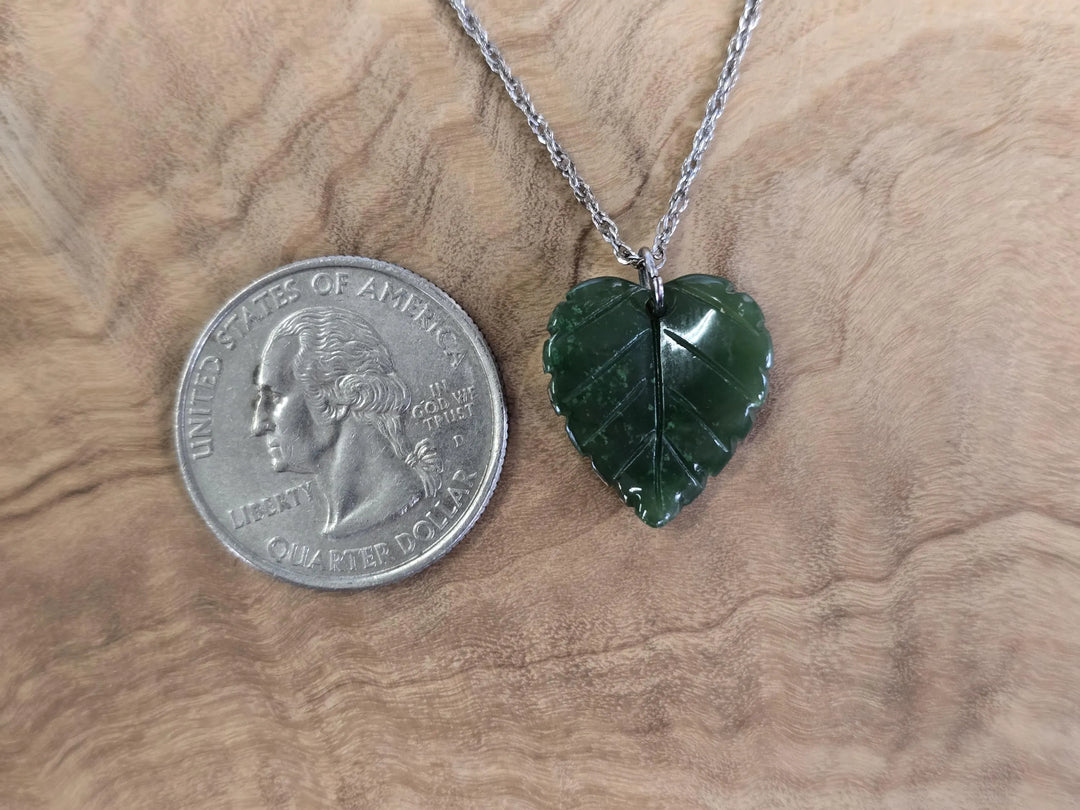 Single Canadian Jade leaf pendant on a silver chain beside a quarter for scale