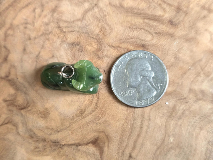 Green nephrite jade water buffalo charm with a silver loop bail beside a quarter on a wood surface