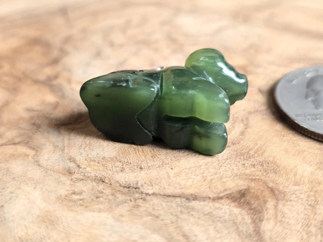 Canadian nephrite jade water buffalo charm with loop on wood surface beside a coin for scale