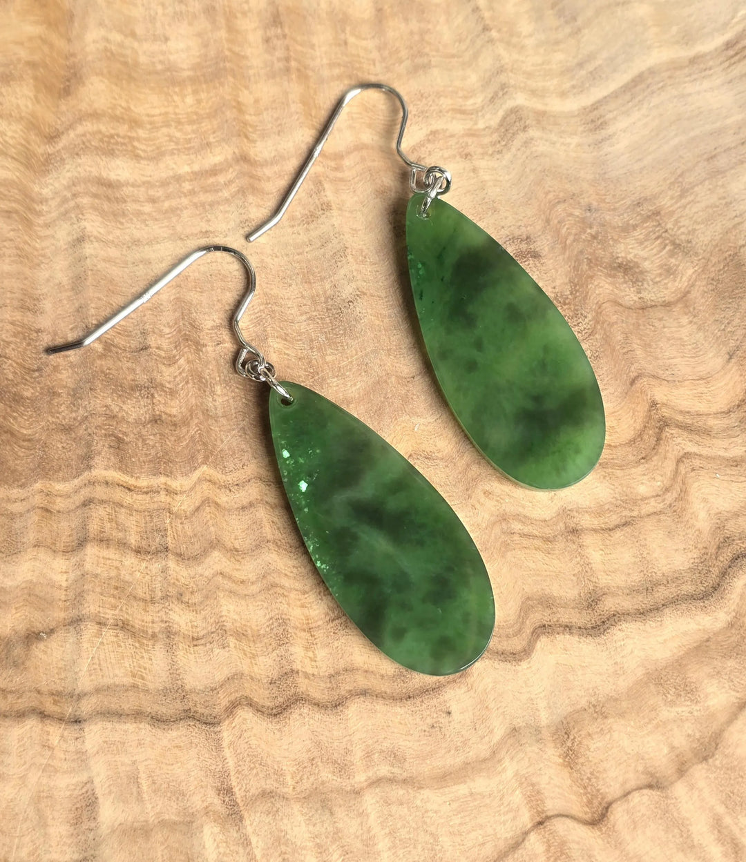 Two green jade teardrop earrings with silver ear wires on a wooden surface