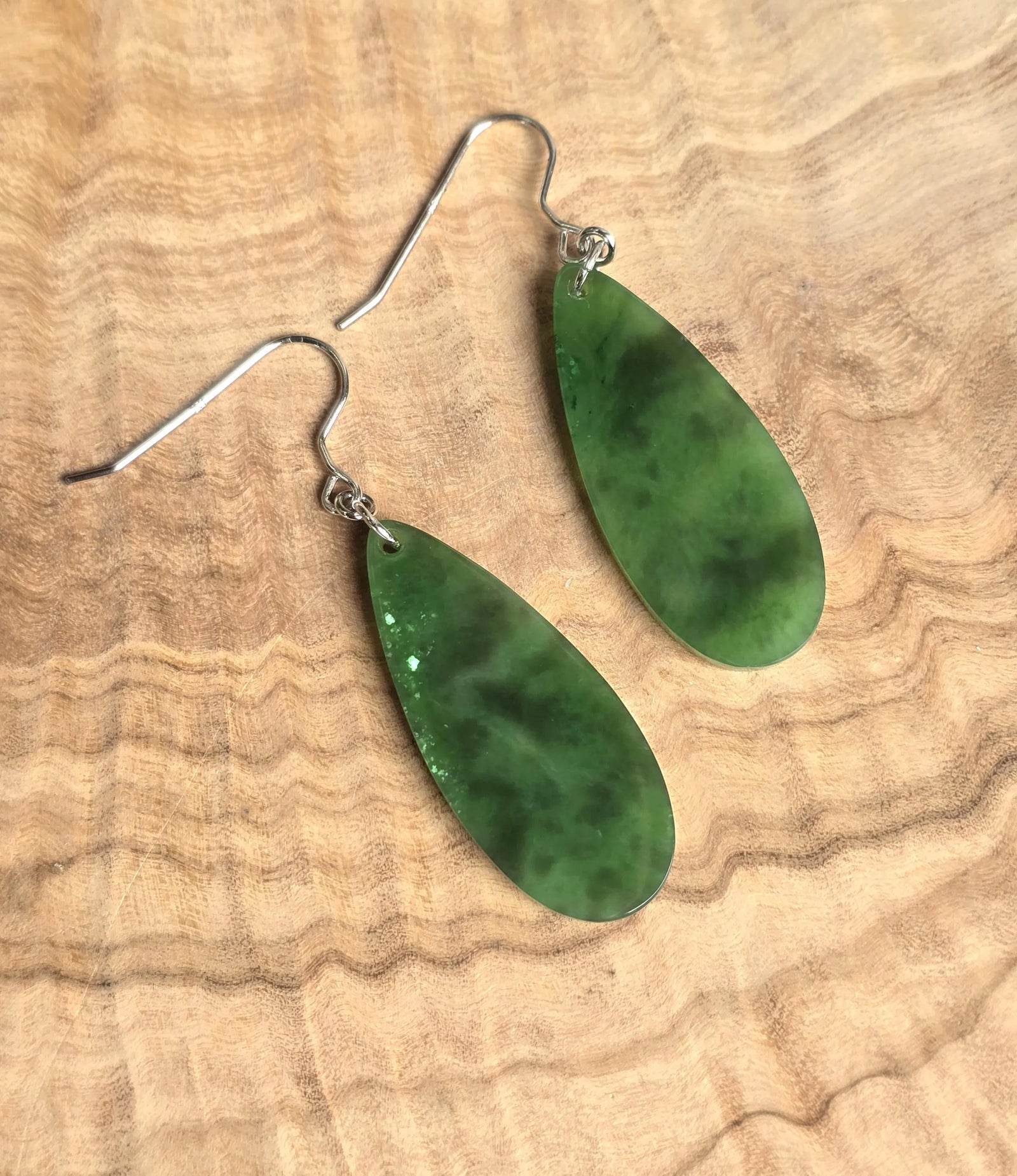 Two green jade teardrop earrings with silver ear wires on a wooden surface
