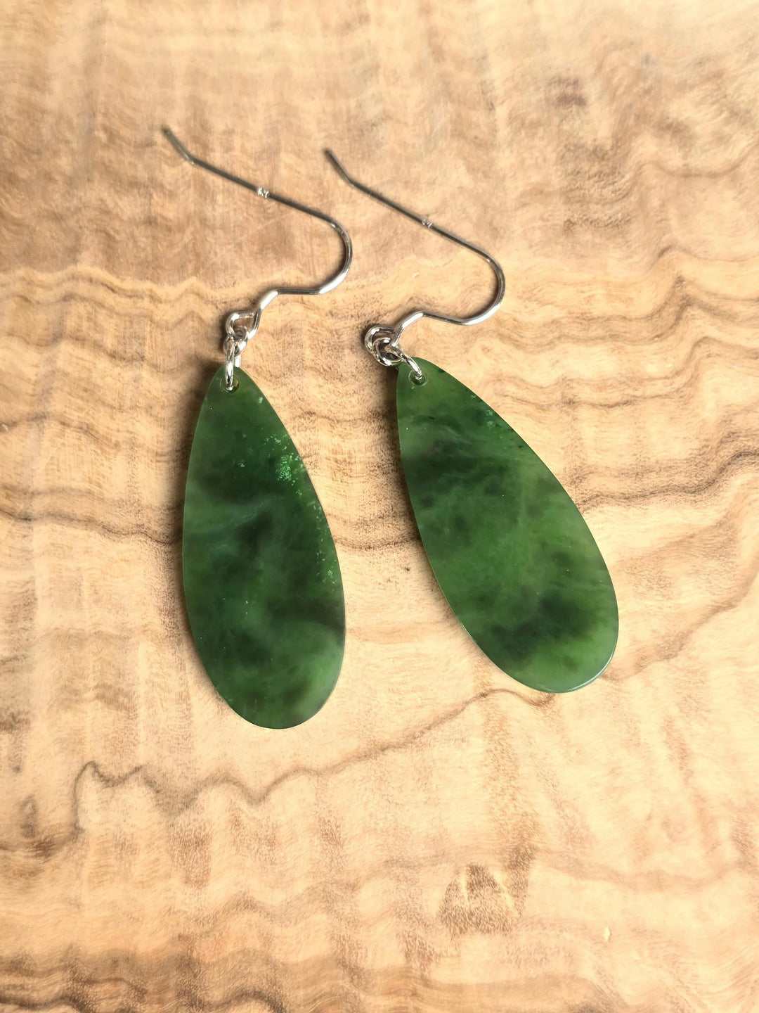 Green jade teardrop earrings with silver hooks on a wooden background