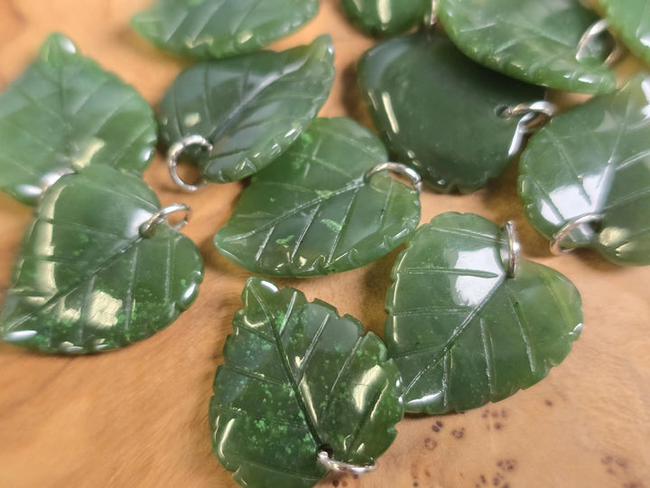 Group of green jade leaf charms with silver bails arranged together.