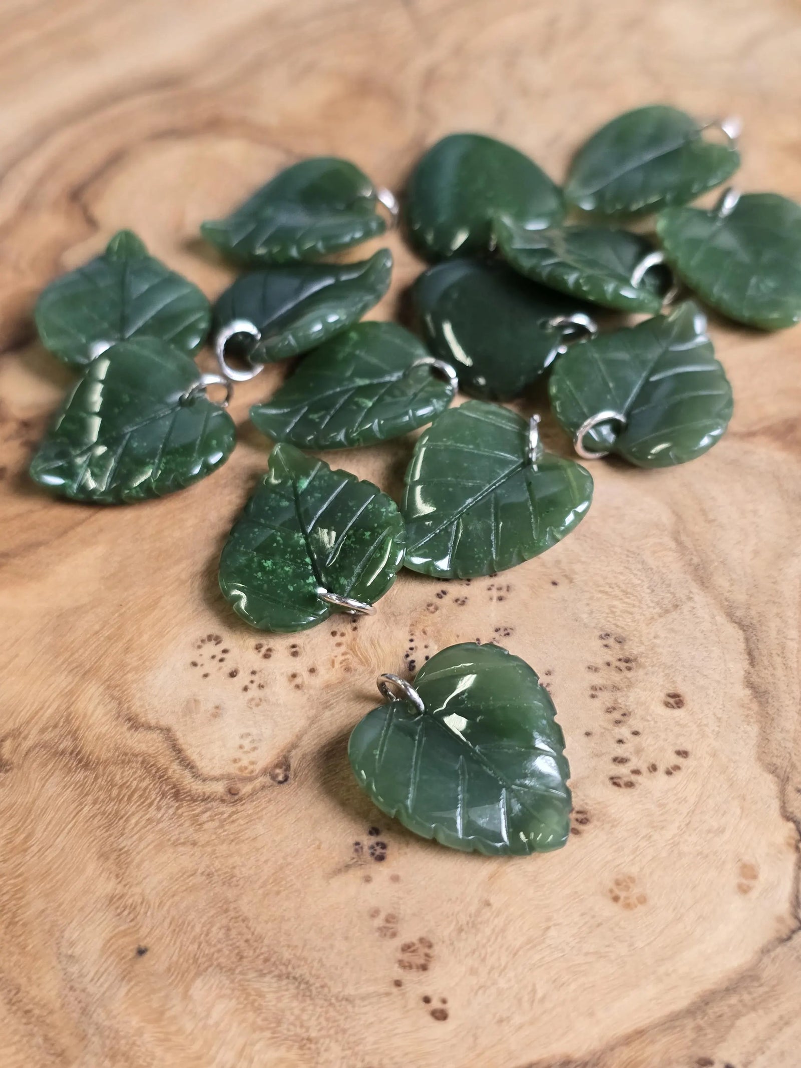 Group of green jade leaf charms with silver loops scattered on wood