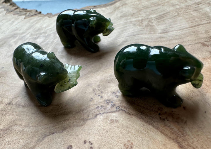 Three dark green jade bear figurines with small jade fish accessories on a wooden surface