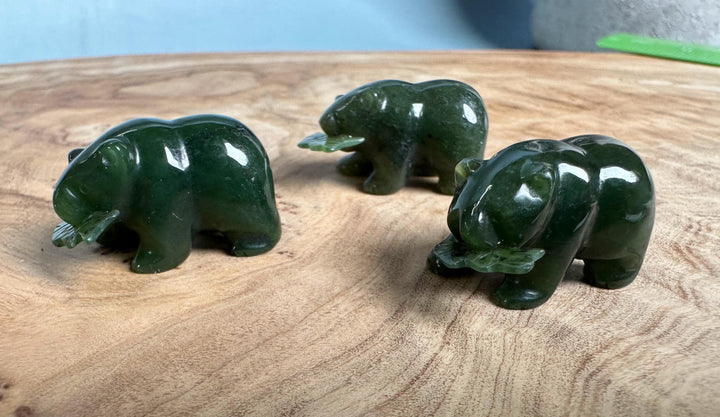 Three dark green jade bear figurines on a wooden surface, one with a jade fish in front