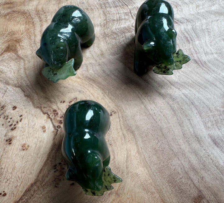 Top view of three green jade bear figurines, each with a jade fish accessory on a wooden surface