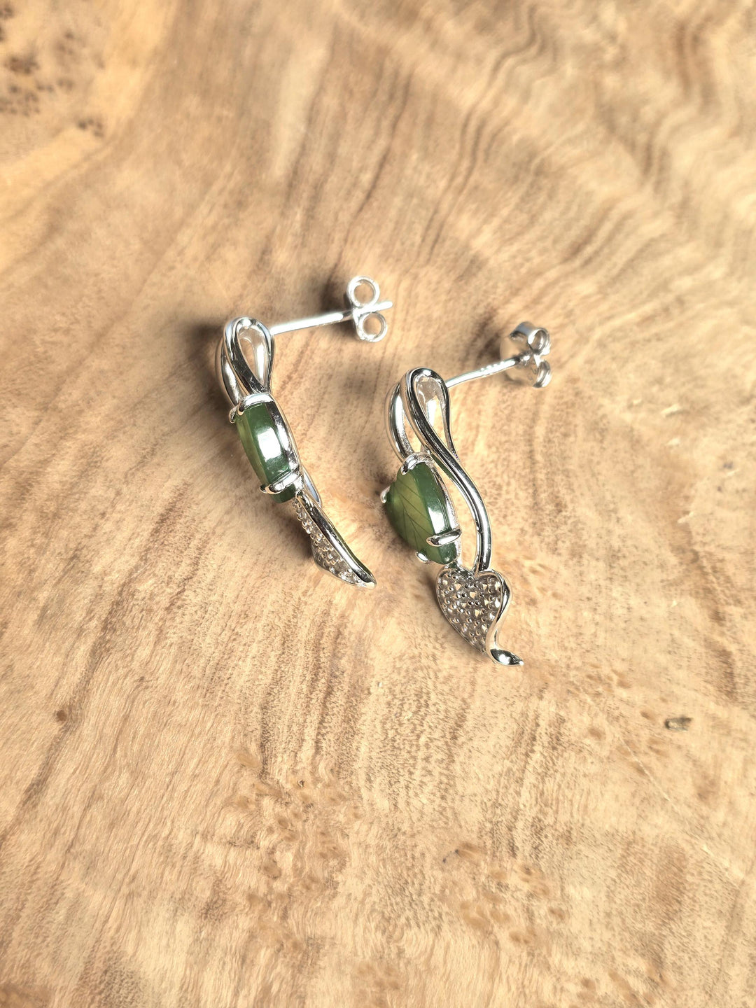 Pair of silver earrings with green gemstones on a wooden surface