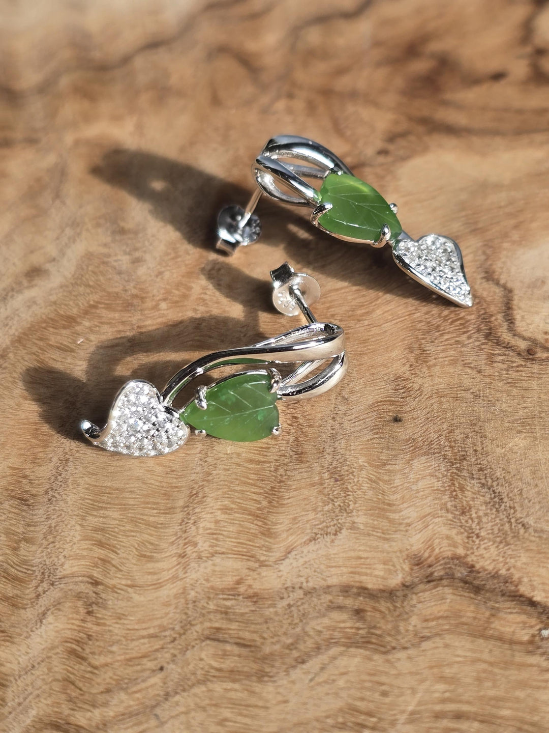 Silver leaf-shaped earrings with green leaves on a wooden surface