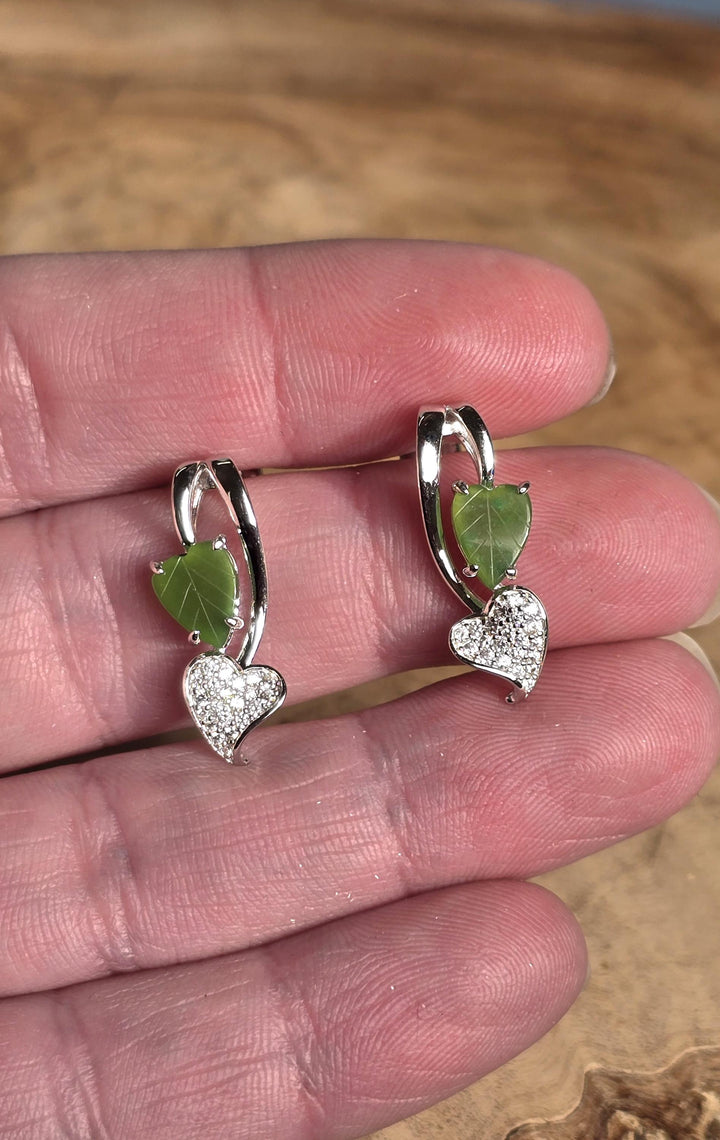 Silver earrings with green leaves held in a hand against a blurred natural background