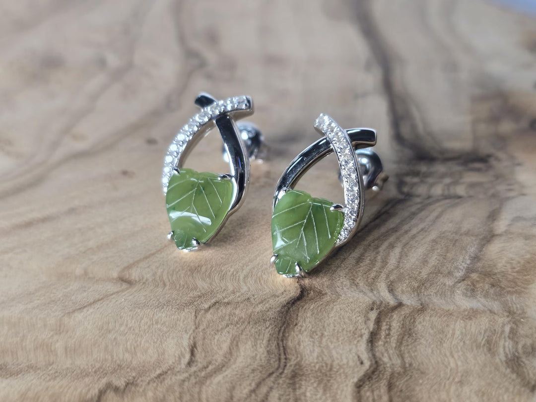 Pair of green leaf-shaped earrings with silver accents on a wooden surface