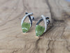 Pair of green leaf-shaped earrings with silver accents on a wooden surface