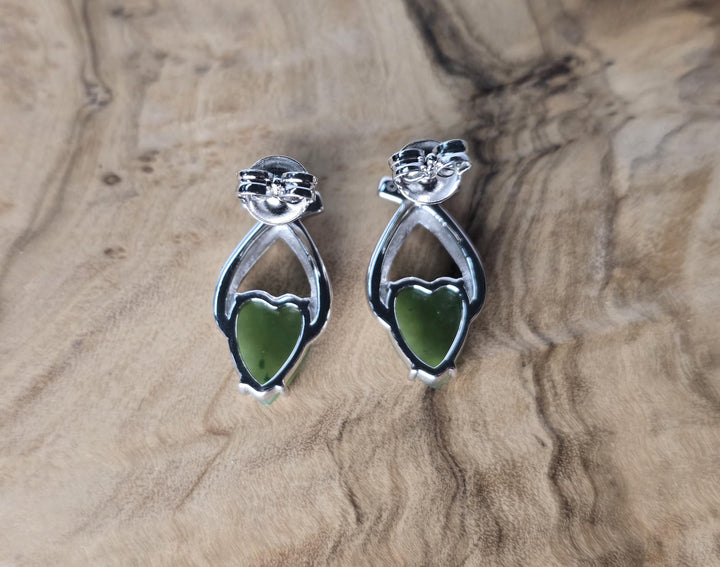 Silver earrings with green heart stones on a wooden surface