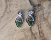 Silver earrings with green heart stones on a wooden surface