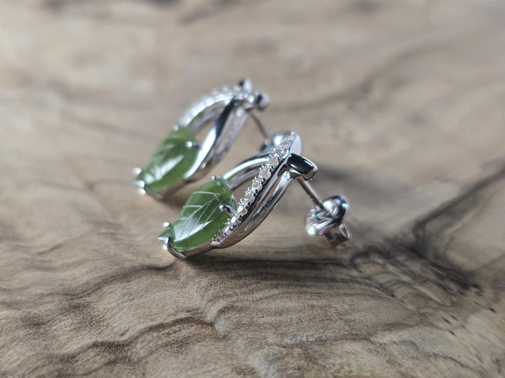 Silver earrings with green leaves on a wooden surface