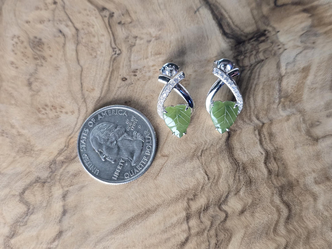 Silver earrings with green leaf design next to a quarter on a wooden surface