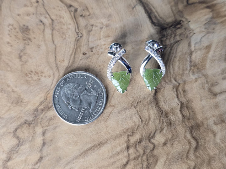 Silver earrings with green leaf design next to a quarter on a wooden surface