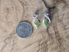 Silver earrings with green leaf design next to a quarter on a wooden surface