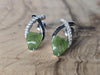 Pair of earrings with green leaf design on a wooden surface