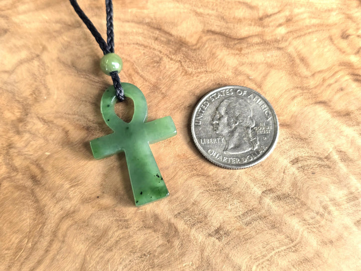 Canadian nephrite jade ankh pendant on a black cord with a small green bead beside a US quarter for scale