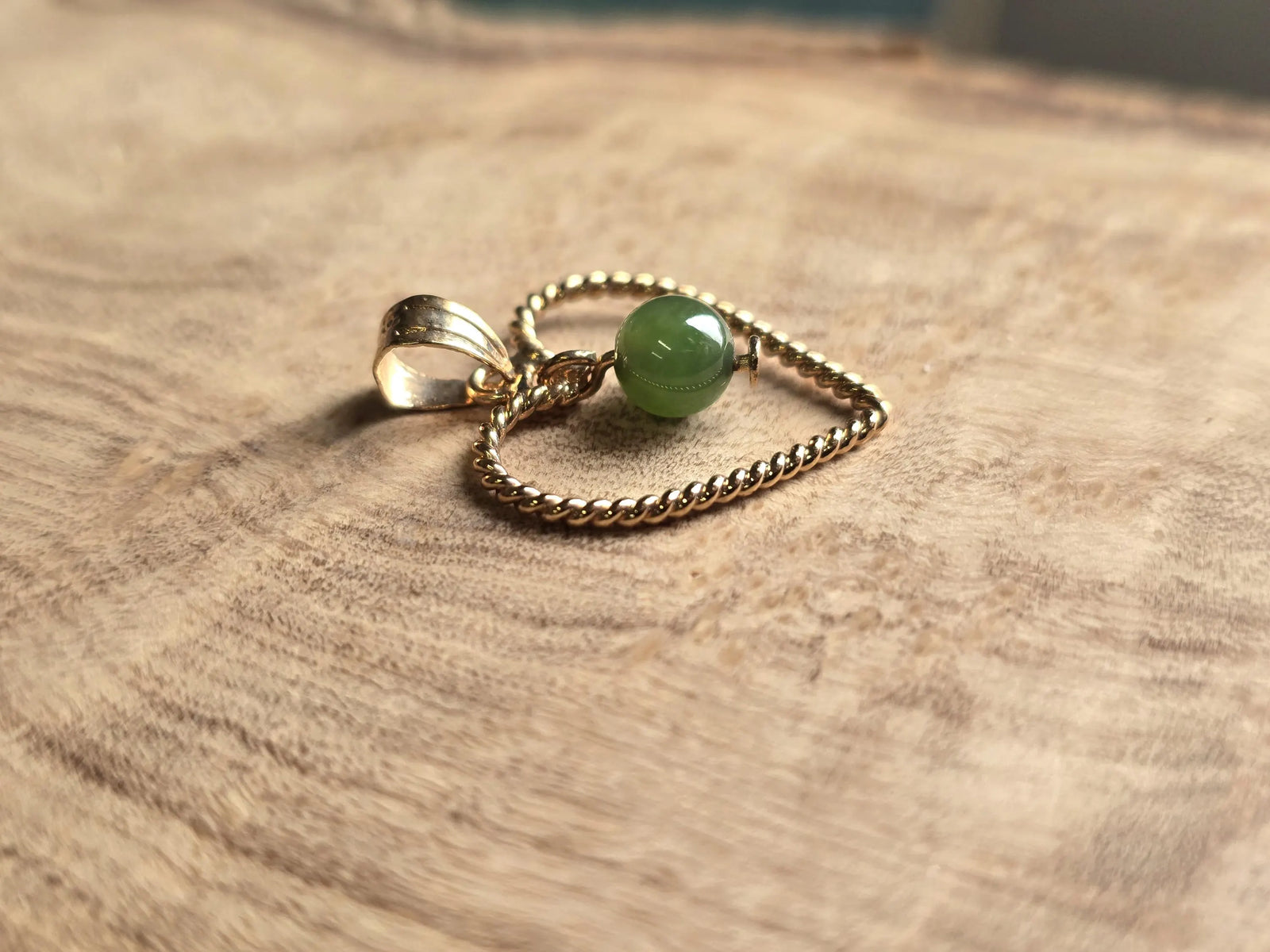 Vintage gold rope heart pendant with green nephrite jade bead on a textured wooden surface
