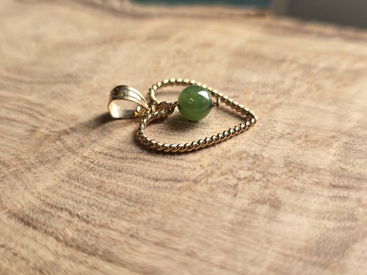 Vintage gold rope heart pendant with green nephrite jade bead on a textured wooden surface