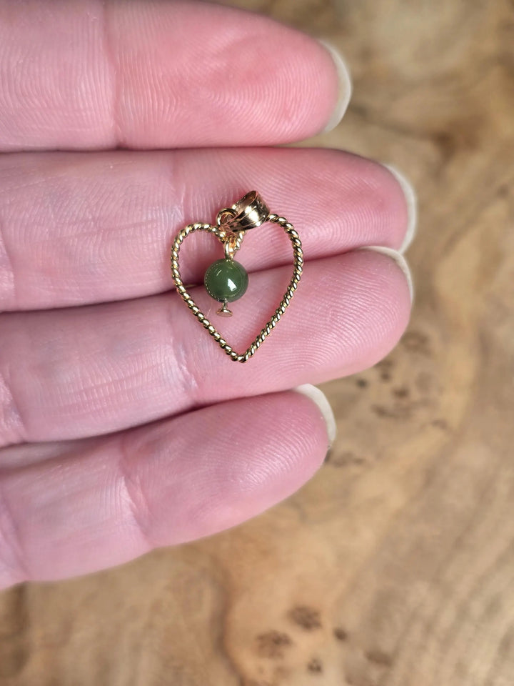 Close up of vintage gold rope heart pendant with a green nephrite jade bead held between fingers