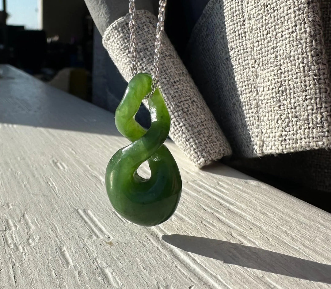 GREEN JADE TWIST HANGING FROM SILVER CHAIN IN DIRECT SUNLIGHT