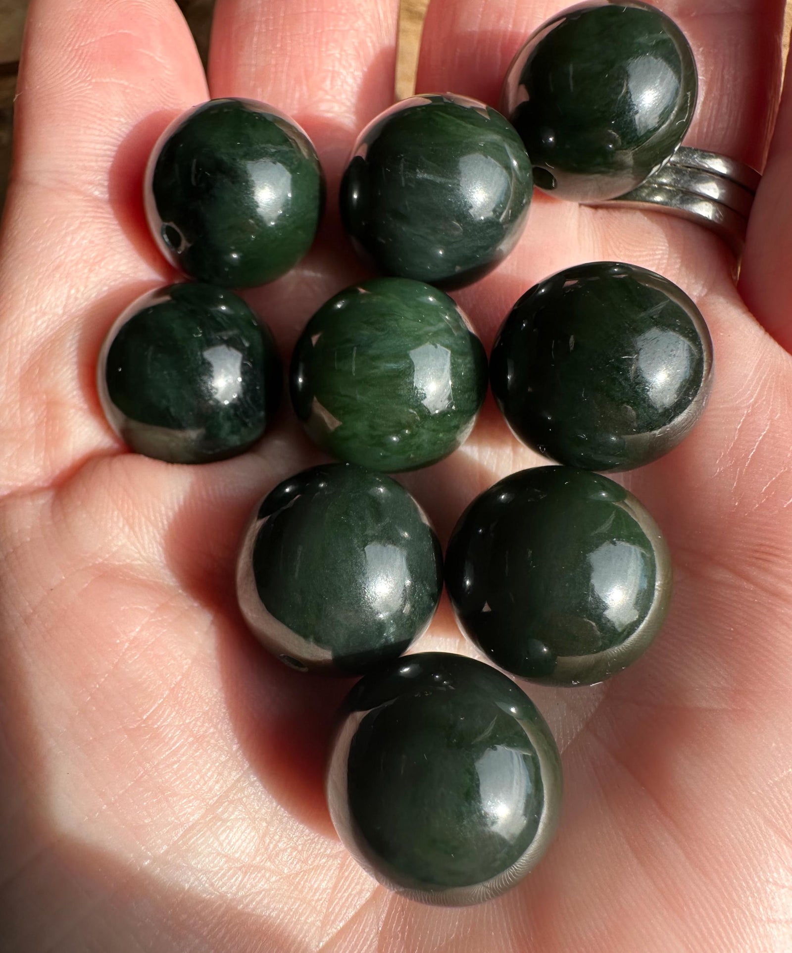 Group of polished dark green nephrite jade beads held in the hand
