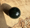 Single 16mm dark green Canadian nephrite jade bead on a beige textured surface