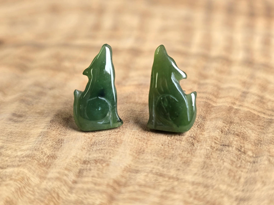 Green jade wolf earrings on a wooden surface