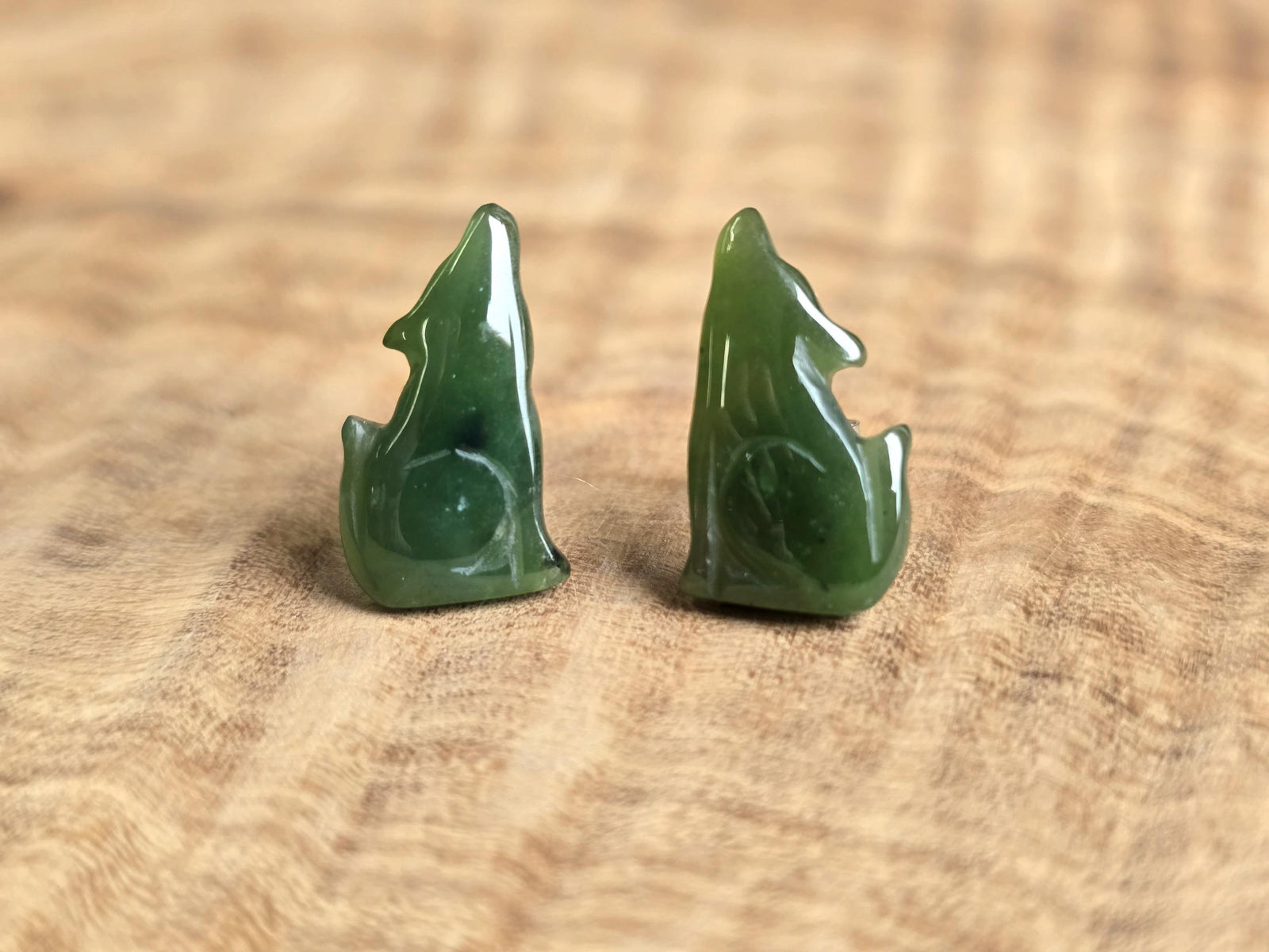 Green jade wolf earrings on a wooden surface