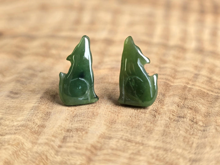 Green jade wolf earrings on a wooden surface