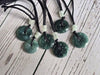Blue Green jadeite pendants on black cords with white beads on a wooden surface
