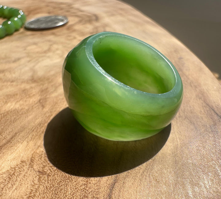 AA Siberian Jade faceted ring in bright green resting on a wooden surface with a green beaded bracelet visible in the background