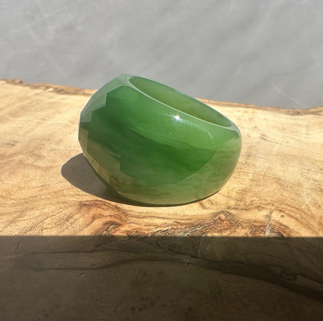 AA Siberian Jade ring in bright green placed on a wooden surface against a pale gray backdrop