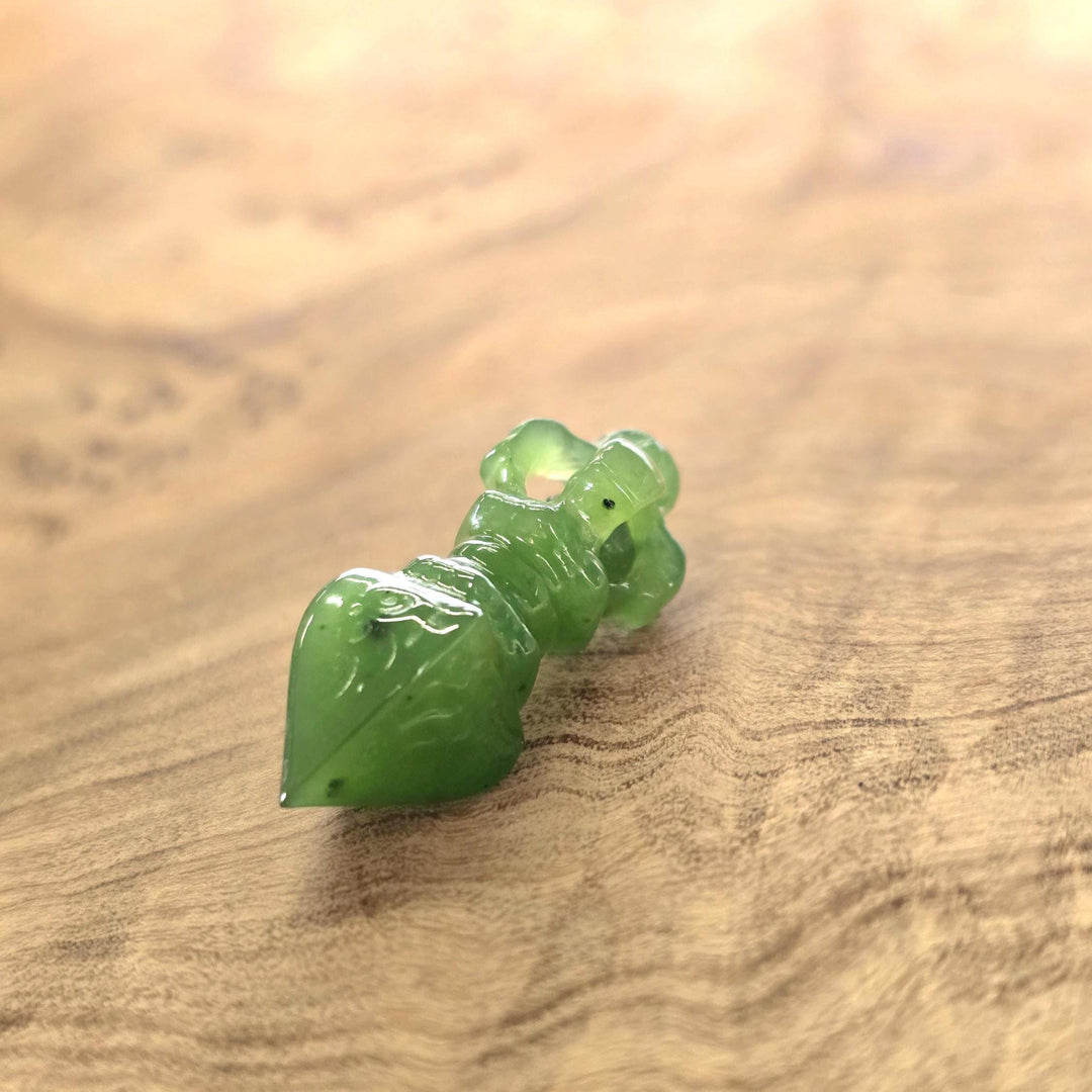A small carved green jade, resting on a warm-toned wooden surface.