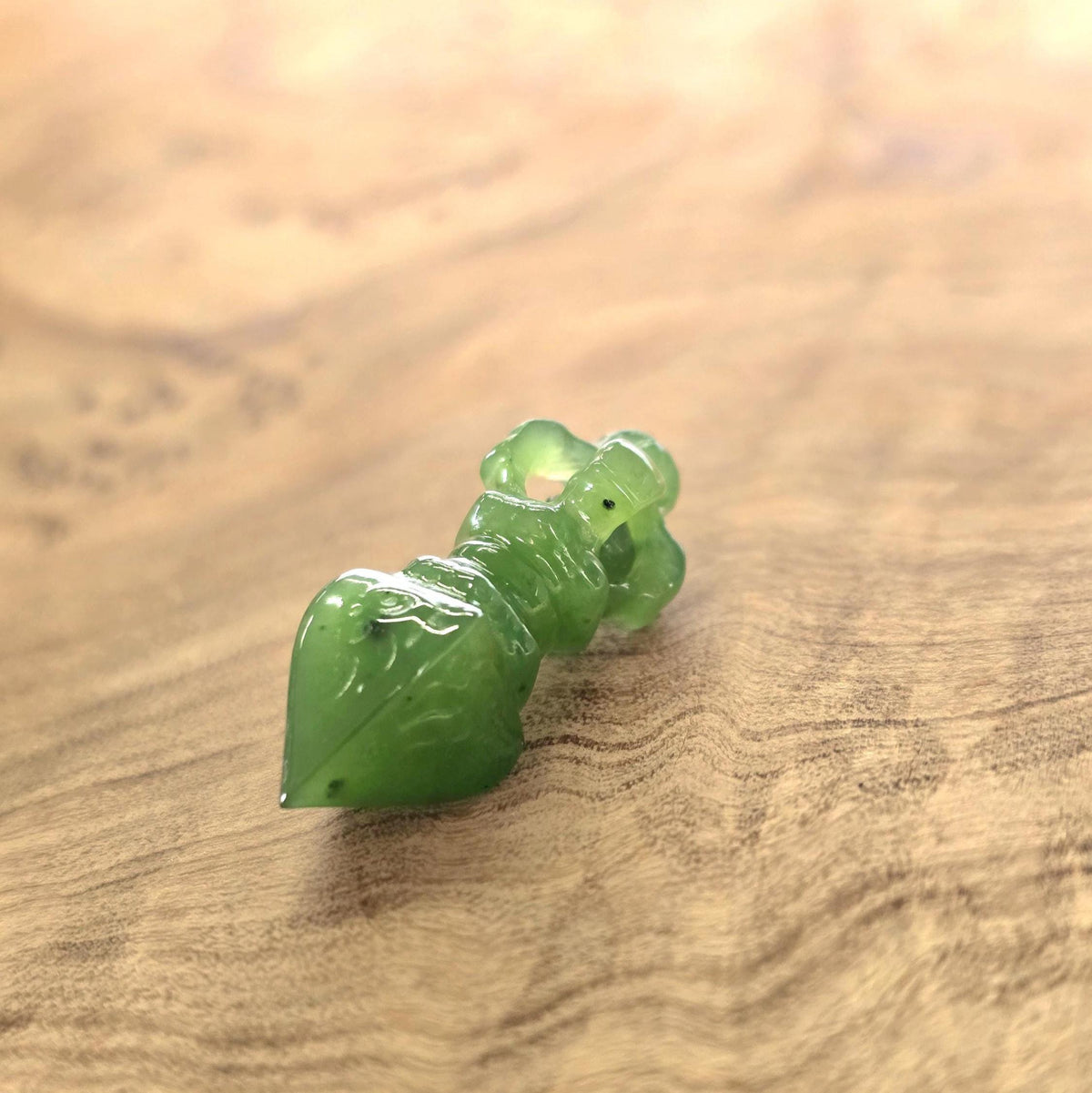 A small carved green jade, resting on a warm-toned wooden surface.