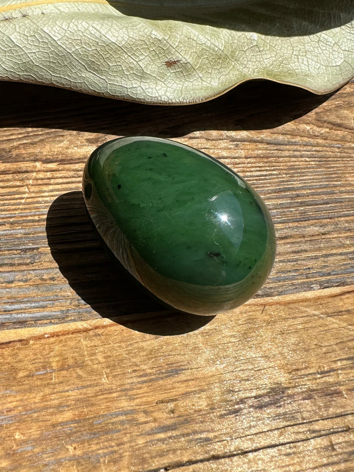 Canadian nephrite yoni egg resting on a wooden surface, glossy green stone with subtle dark inclusions
